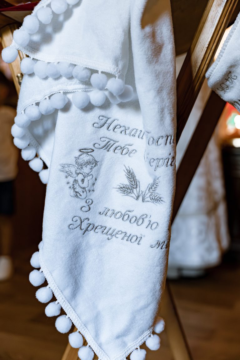 Білий хрестильний рушник з вишитим благословенням і декоративними помпонами