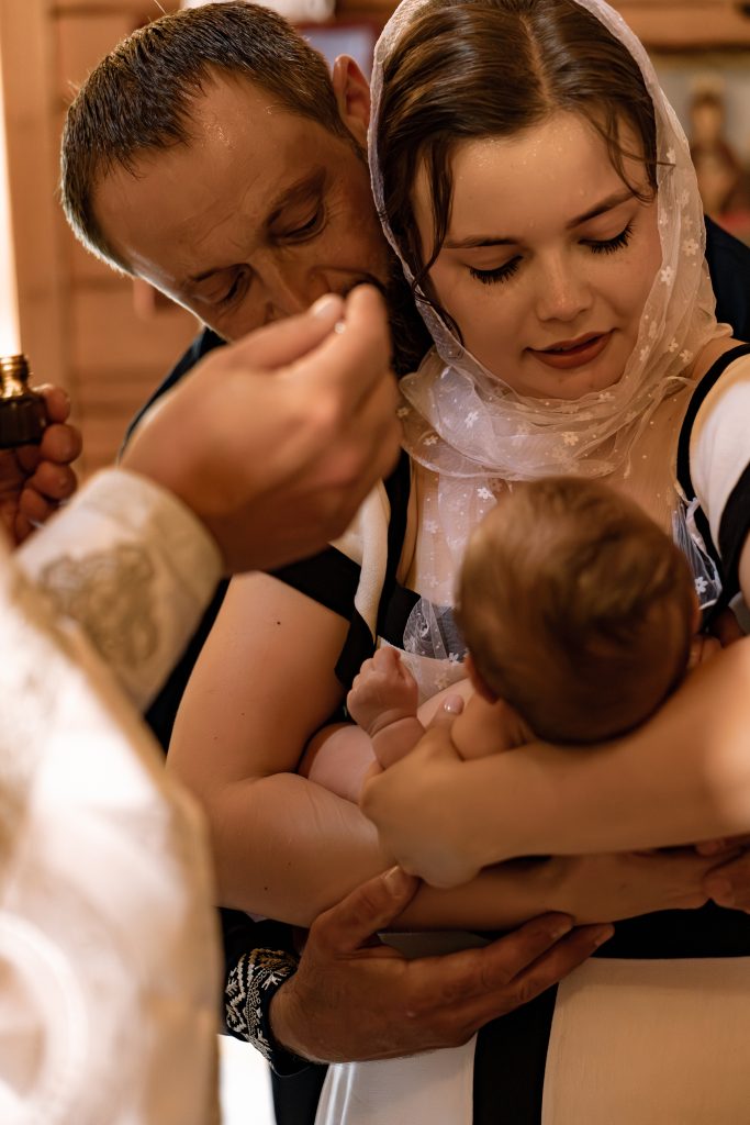Чоловік і жінка тримають Тимофія під час Таїнства Хрещення, поки священник здійснює обряд