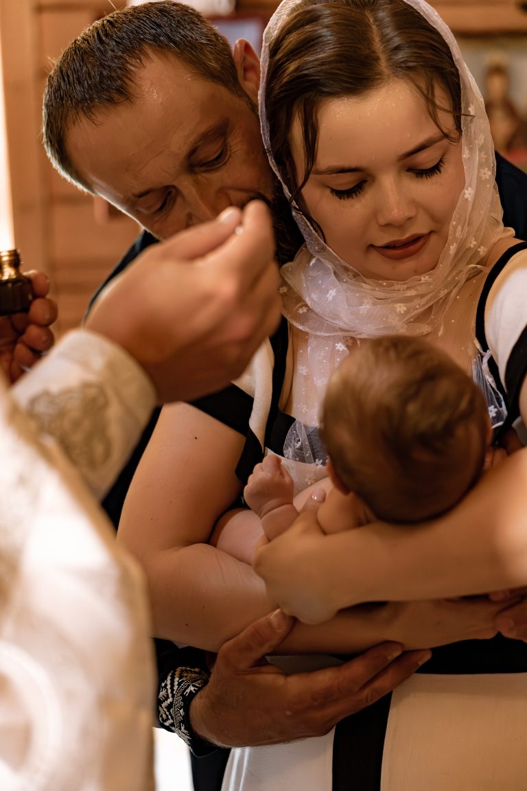 Чоловік і жінка тримають Тимофія під час Таїнства Хрещення, поки священник здійснює обряд