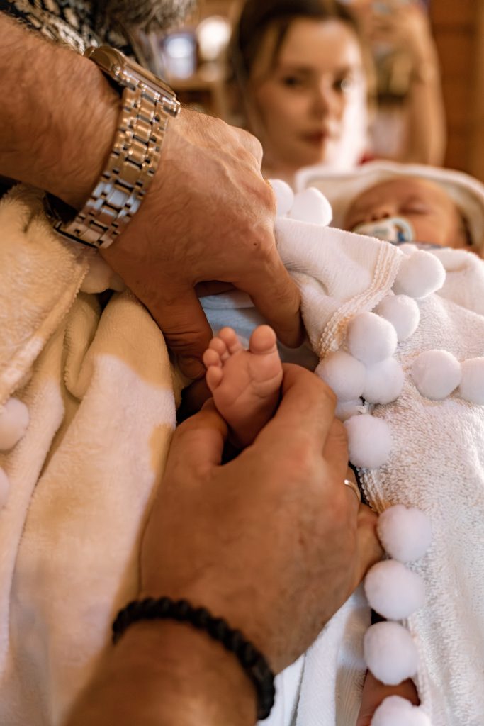 Крупний план ніжок Тимофія, загорнутого у білий хрестильний рушник, у руках дорослих