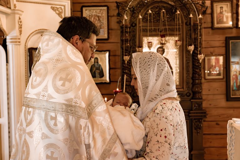 Священник і жінка у білій хустці тримають загорнутого Тимофія біля ікон