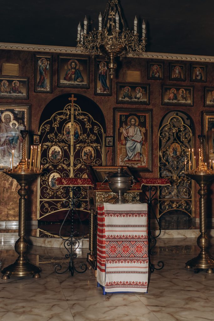 Металева купіль на столі з вишитим рушником і запаленими свічками у храмі