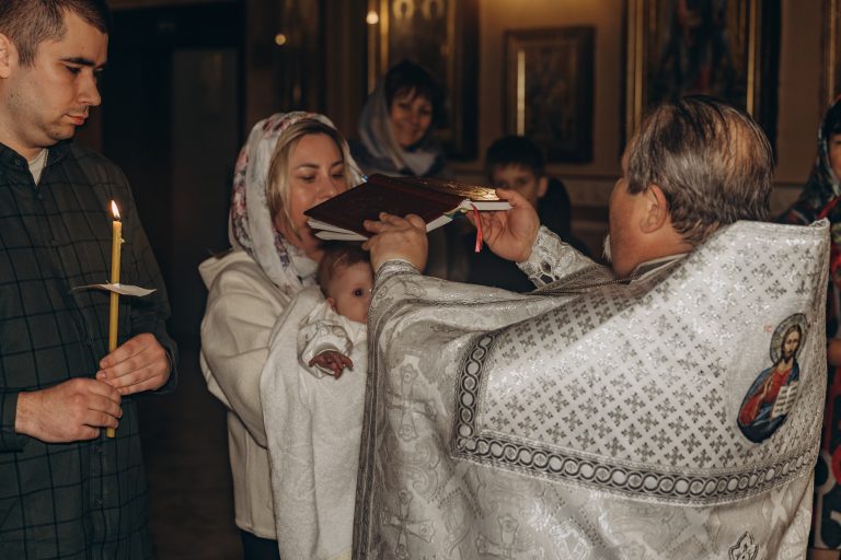 Священник тримає богослужбову книгу над жінкою з Олександром, поруч чоловік зі свічкою