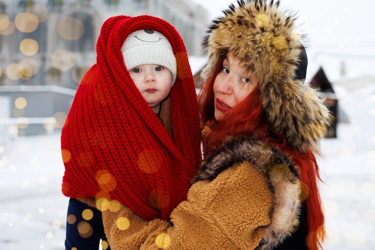 Крупний портрет жінки та маленької дитини, загорнутої у червоний в'язаний шарф, на зимовій площі