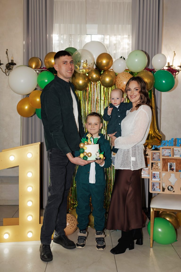 Двоє дорослих і двоє хлопчиків позують з тортом біля святкової фотозони
