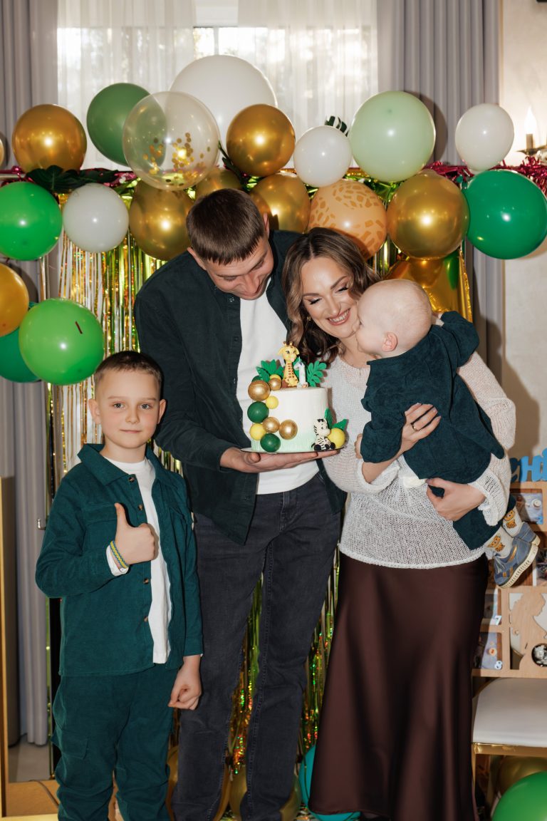 Четверо учасників свята тримають торт і дивляться на Олексія біля фотозони