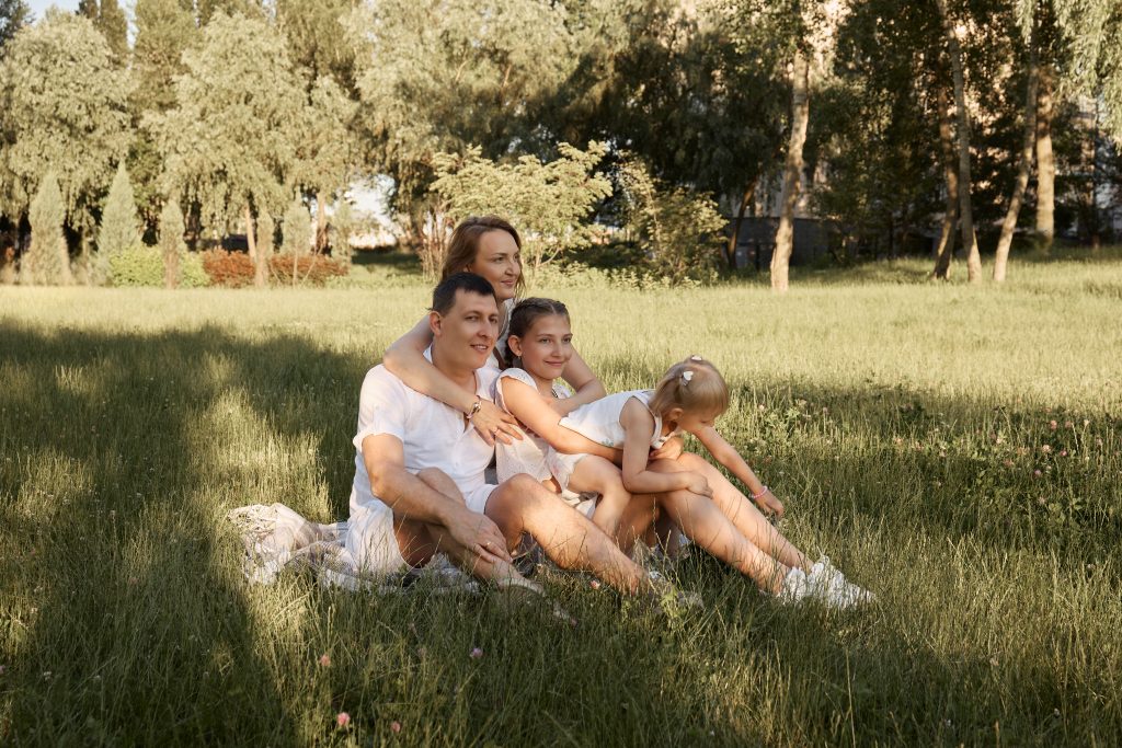 Родина з двома дівчатками сидить разом на пледі у високій траві