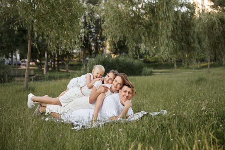 Родина лежить один за одним на пледі у високій траві та дивиться в камеру