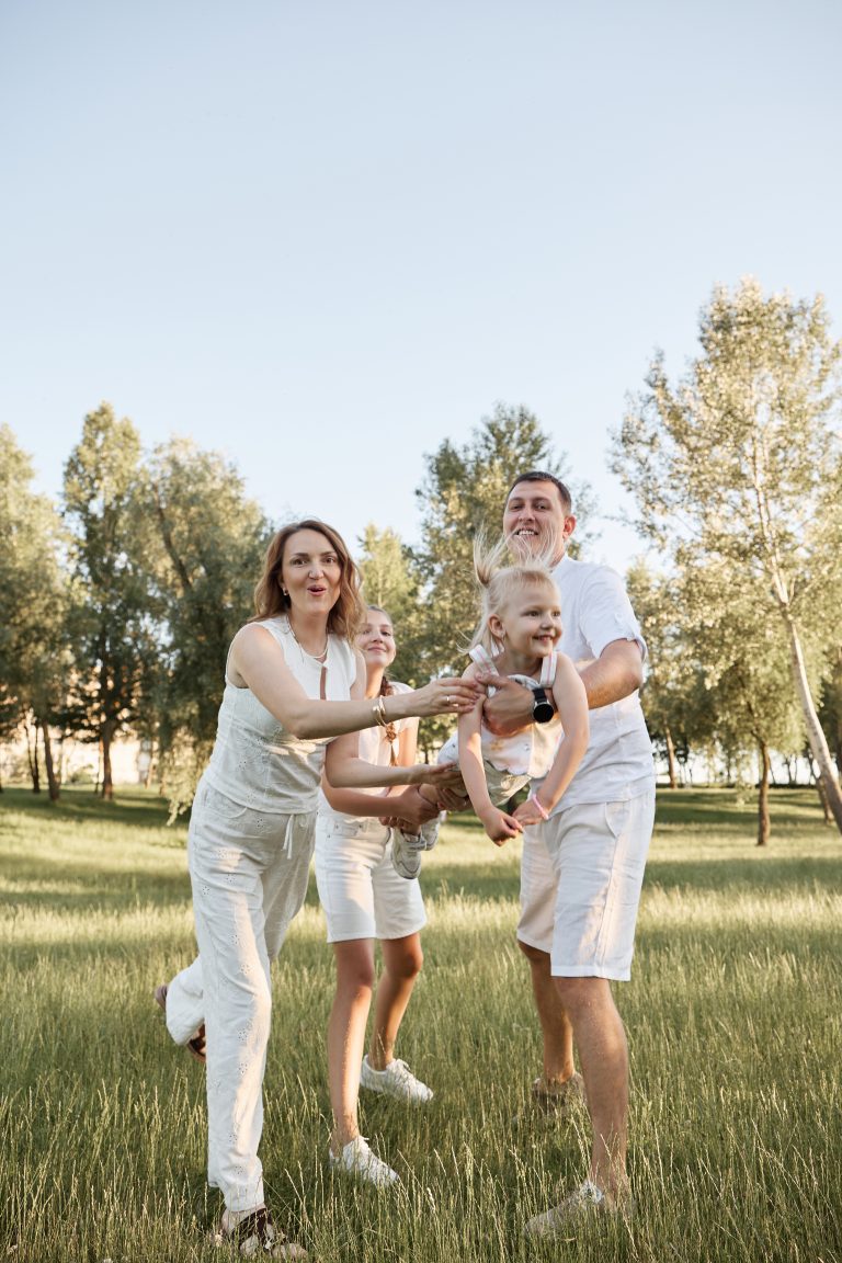 Родина грається з маленькою дівчинкою у високій траві під час прогулянки