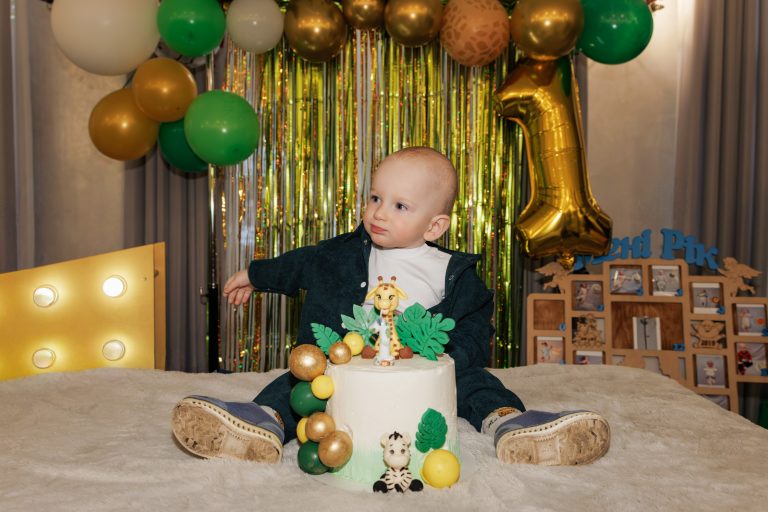 Олексій сидить перед тортом на тлі кульок, цифри один і фоторамки