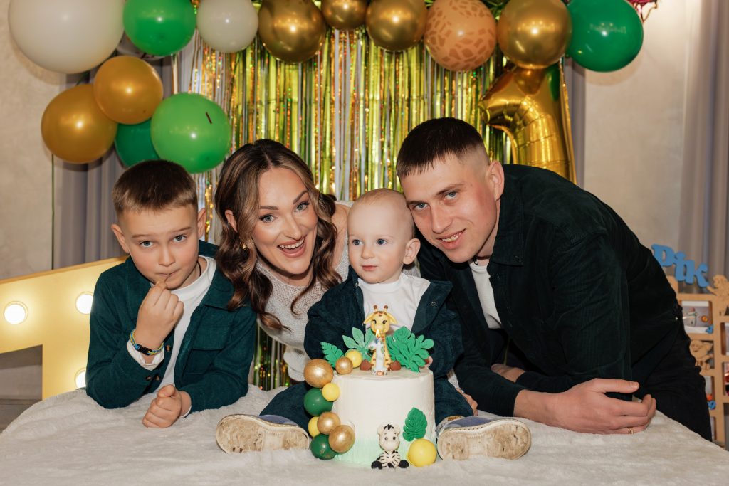 Олексій з двома дорослими і старшим хлопчиком позує біля торта зі свічкою