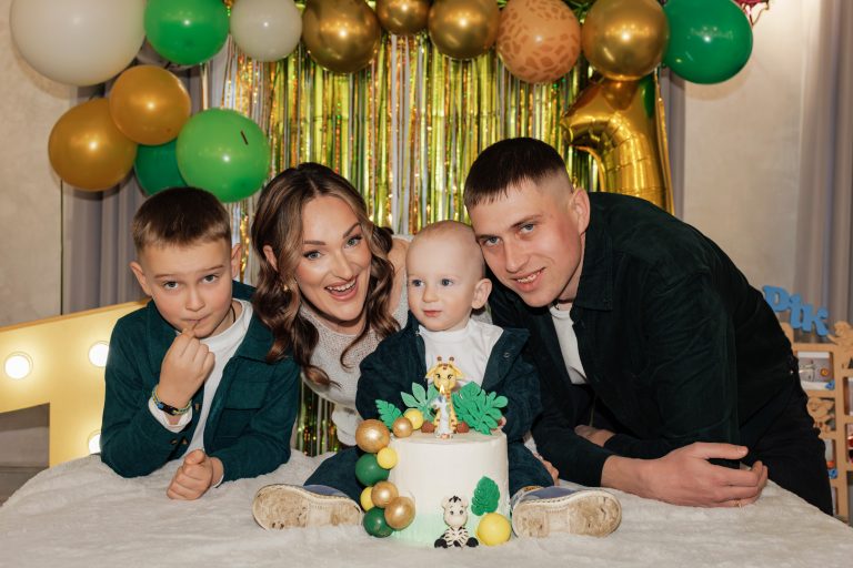 Олексій з двома дорослими і старшим хлопчиком позує біля торта зі свічкою