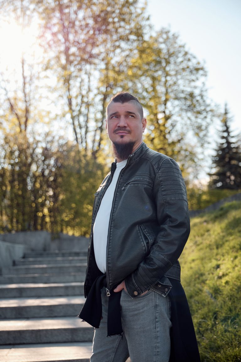 Чоловік у шкіряній куртці стоїть на сходах у сонячному парку