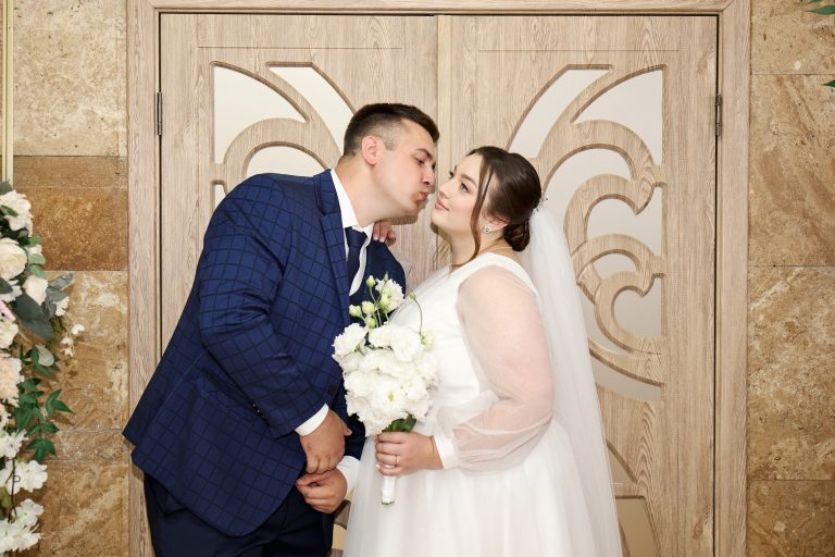 Максим нахиляється до Наталі для поцілунку біля декоративних дверей РАЦСу