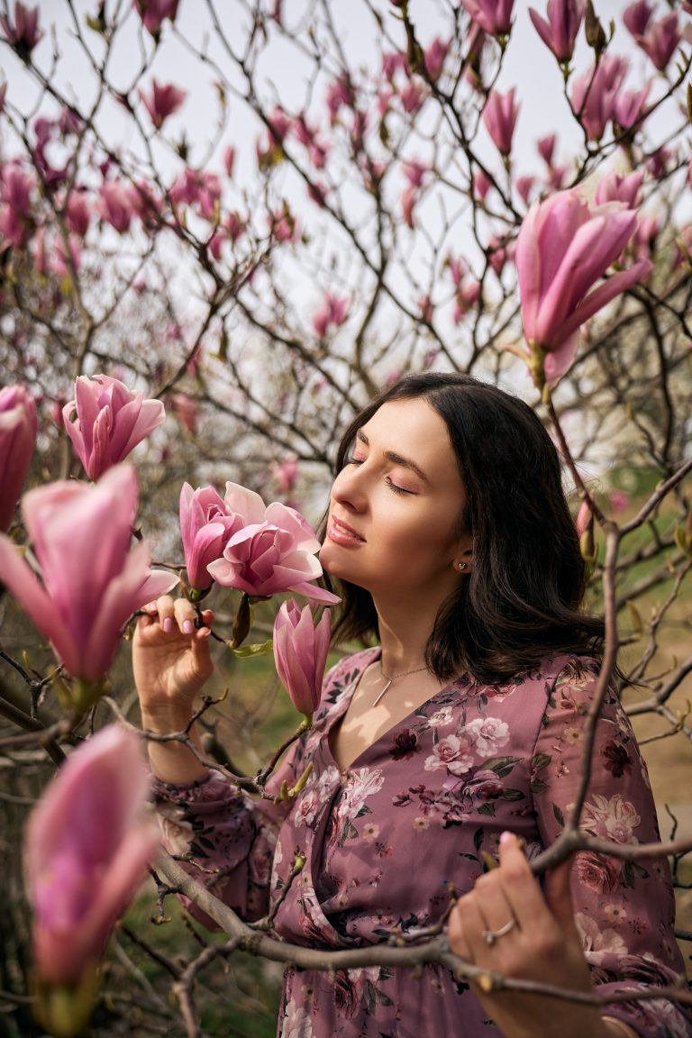 Ірина із заплющеними очима стоїть серед рожевих магнолій у квітковій сукні