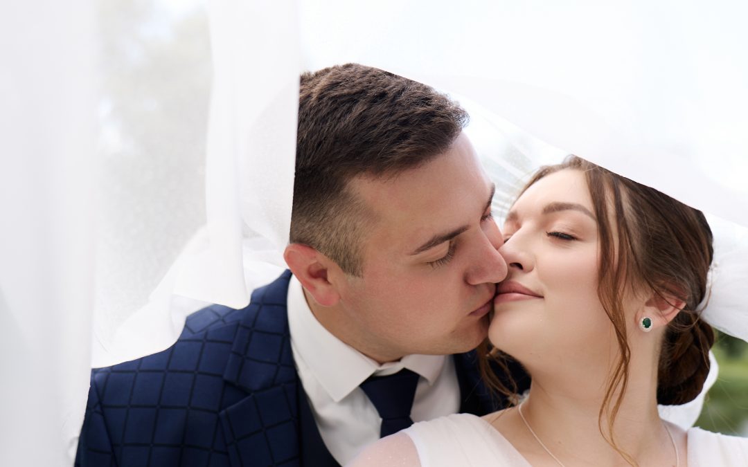 Максим цілує Наталі під легкою білою фатою в парку, весільна фотосесія, Київ