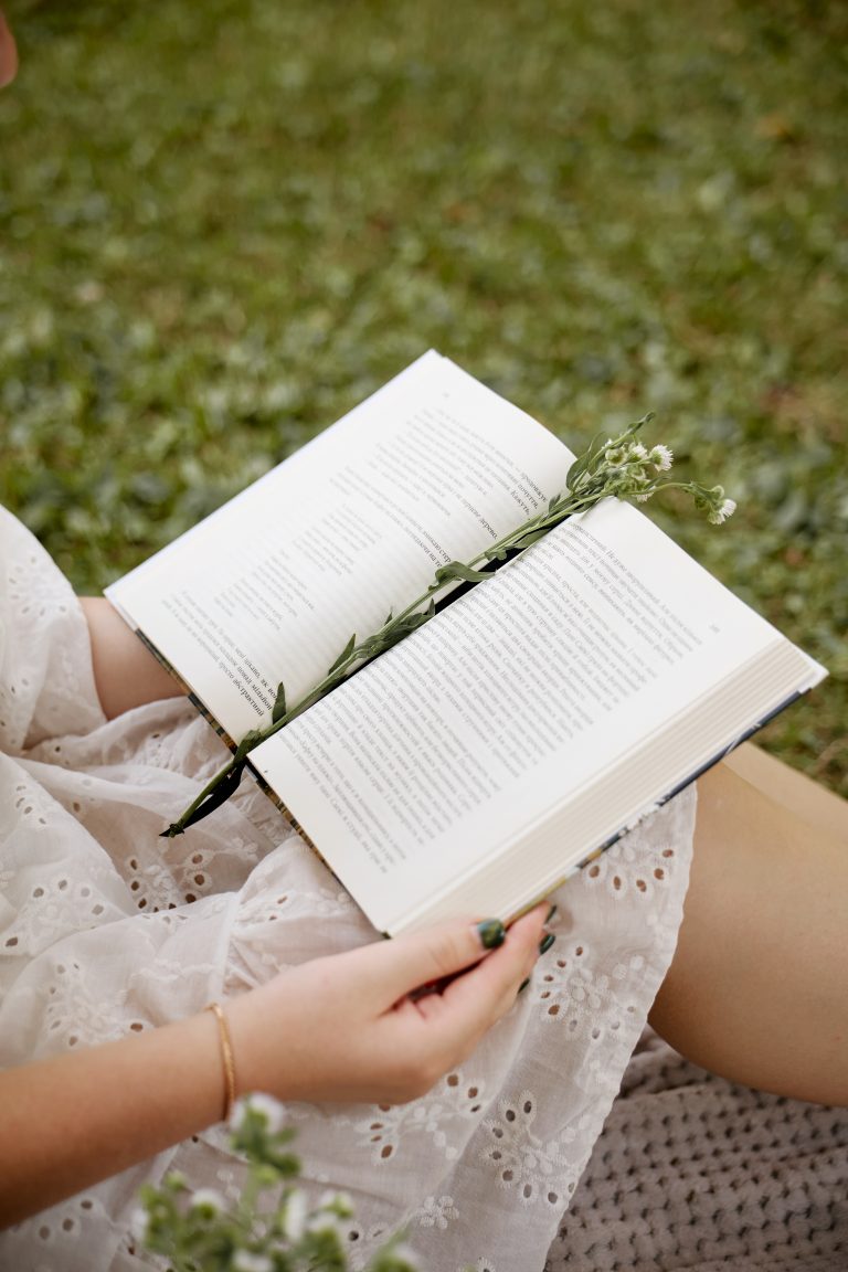 Відкрита книжка з польовою квіткою лежить на колінах Аліси під час пікніка в парку