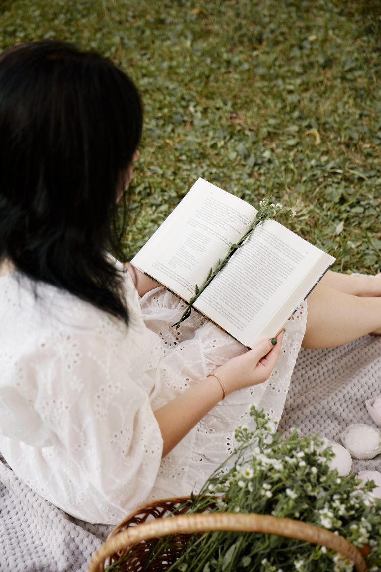 Аліса читає відкриту книжку на пледі поруч із кошиком польових квітів