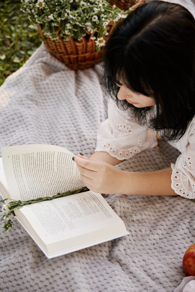 Крупний план Аліси, яка читає відкриту книжку лежачи на світлому пледі