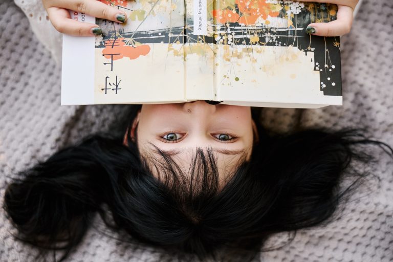 Креативний портрет Аліси лежачи, де книжка закриває частину обличчя