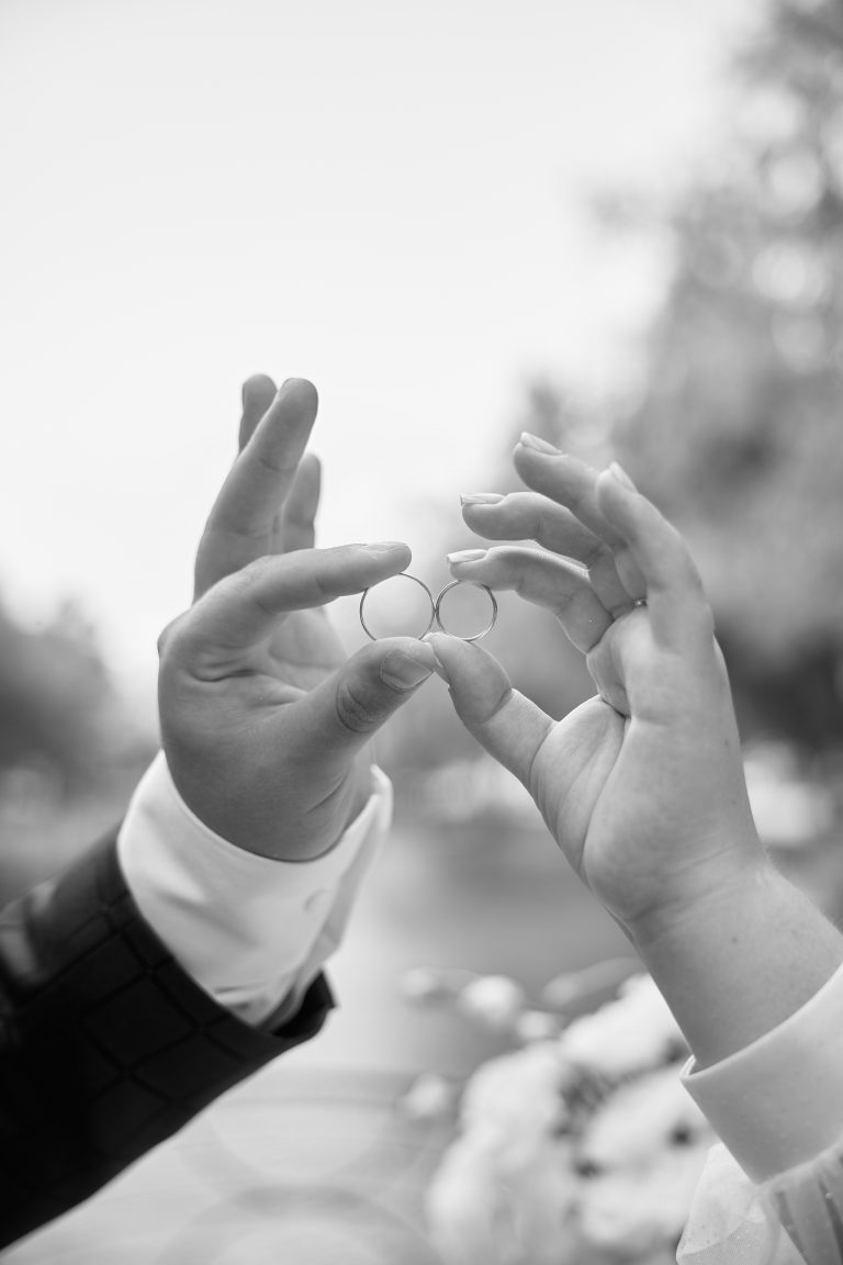 Руки Наталі та Максима тримають дві обручки на тлі парку