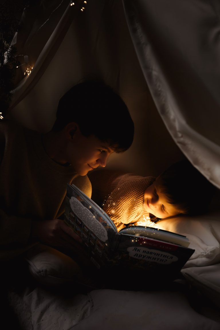 Двоє хлопців читають книжку під ковдрою при теплому світлі гірлянди