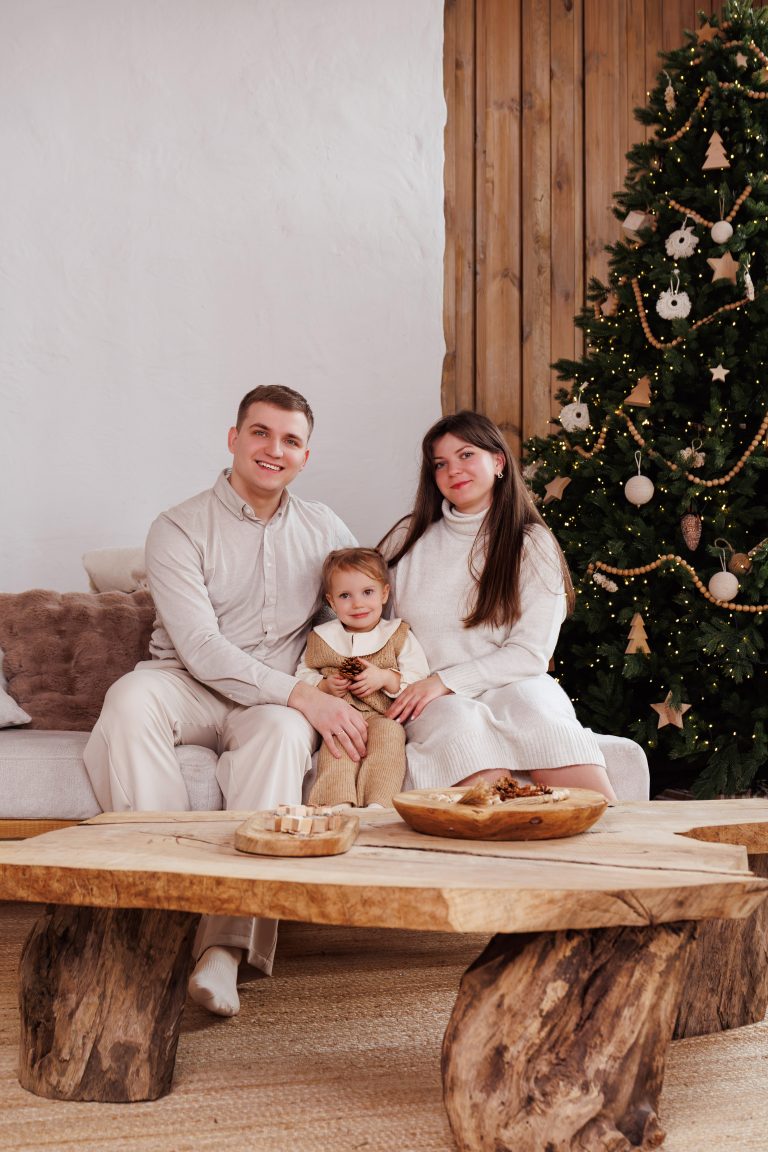Сім'я з маленькою дитиною сидить на світлому дивані біля новорічної ялинки