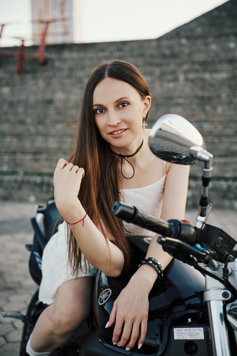Жінка з довгим темним волоссям усміхається, сидячи на чорному мотоциклі