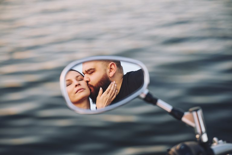 Поцілунок пари відображається у дзеркалі мотоцикла на тлі води