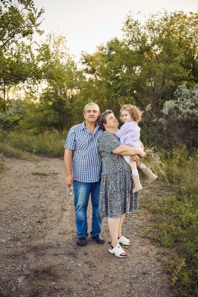 Бабуся тримає маленьку дівчинку на руках поруч із дідусем на лісовій стежці