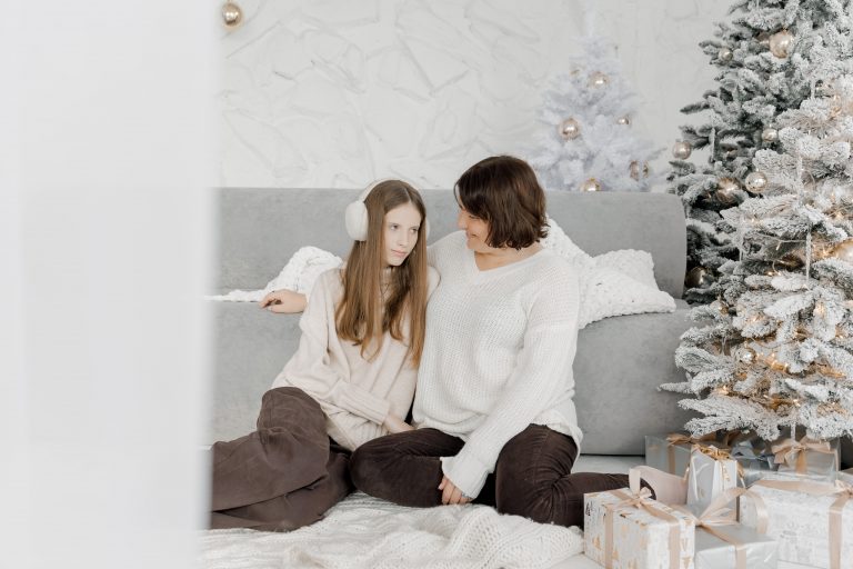 Мама Тетяна та донька Дарина сидять біля засніженої ялинки у світлій новорічній студії