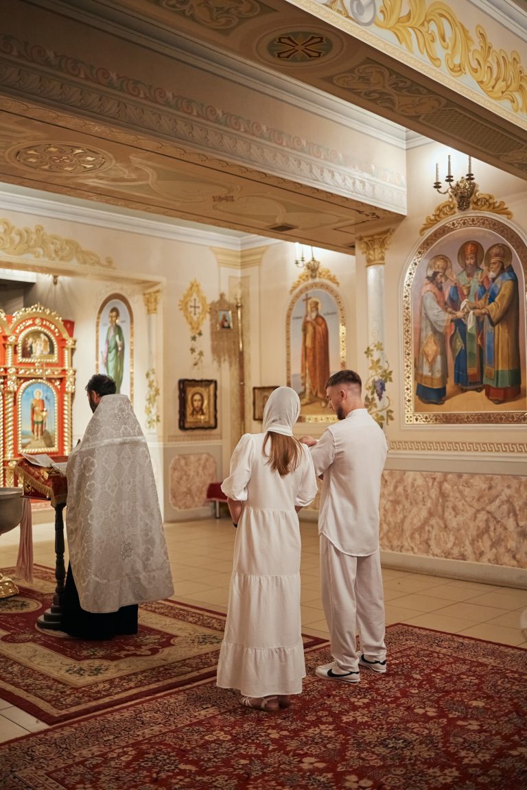 Священник проводить обряд у храмі, поруч стоять чоловік і жінка в білому одязі