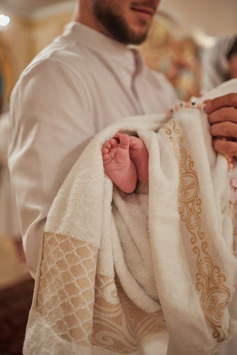 Маленькі стопи немовляти визирають з білого рушника під час хрещення