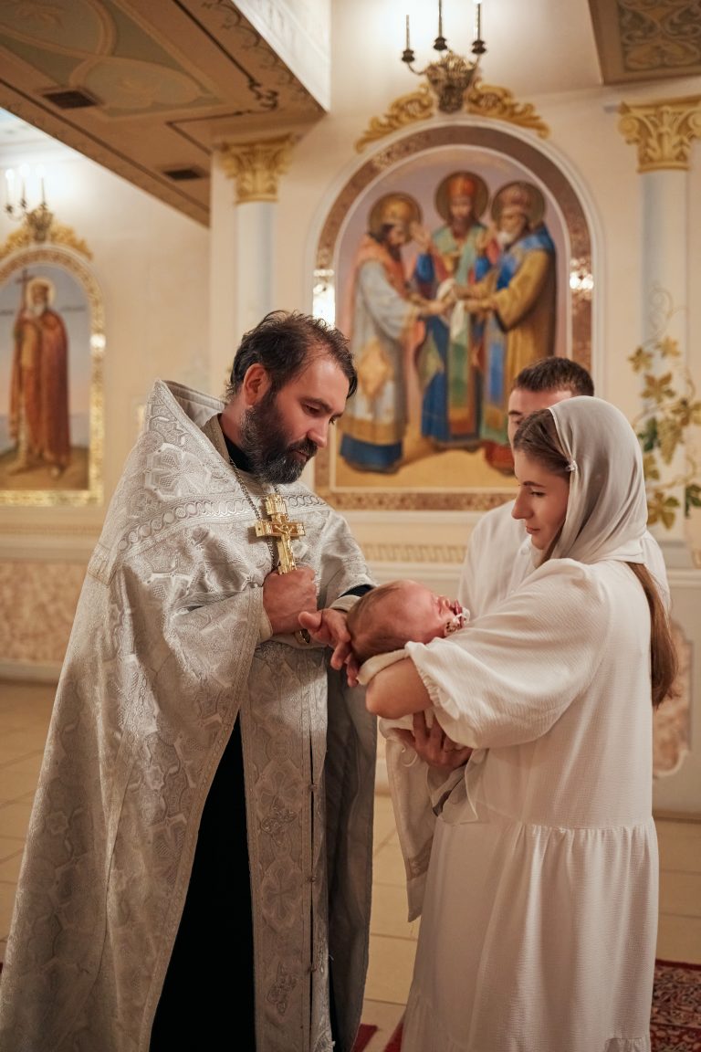 Священник тримає хрест біля Емілії, яку тримає жінка в білому одязі