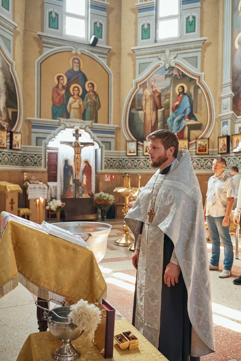 Священник стоїть біля хрестильної купелі в інтер'єрі православного храму