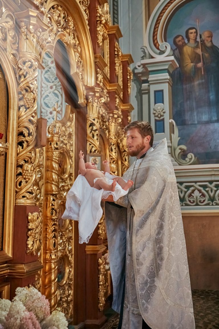 Священник тримає немовля біля золотого іконостаса у православному храмі