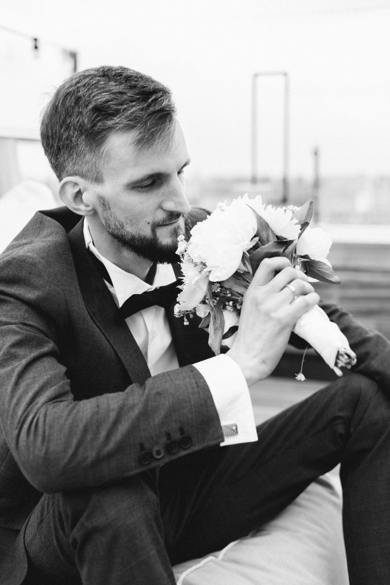 Чорно-білий портрет Олексія, який сидить у костюмі та тримає весільний букет