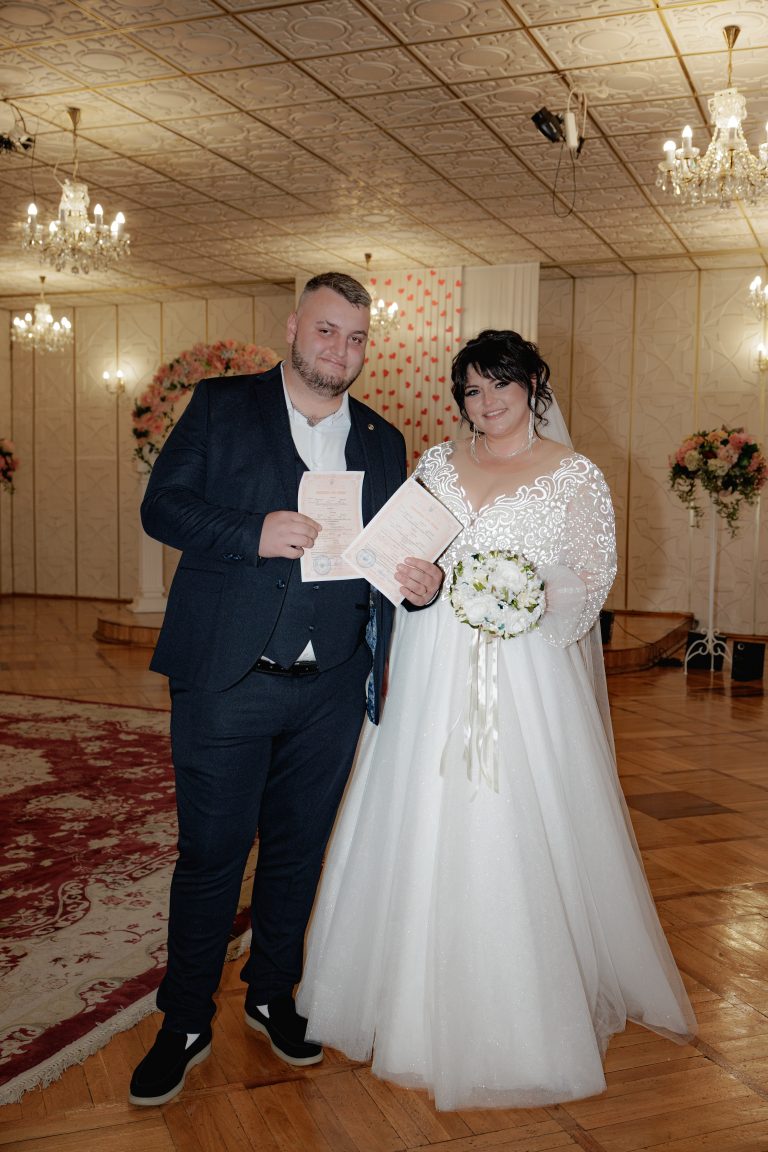 Наталя і Влад позують із документами про шлюб і білим весільним букетом