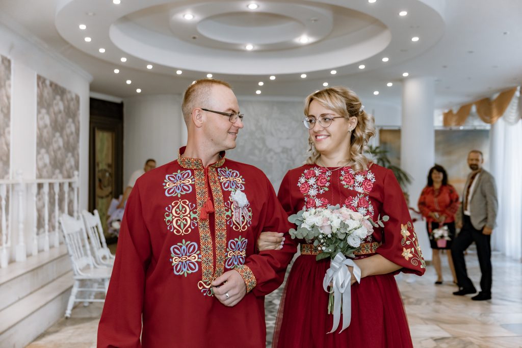 Марина та Ігор ідуть разом залом Дніпровського РАЦСу в бордових етнічних весільних образах