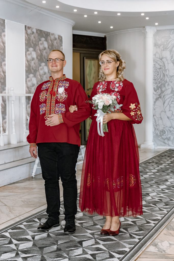 Марина та Ігор стоять поруч у залі Дніпровського РАЦСу в бордовому вбранні з українською вишивкою