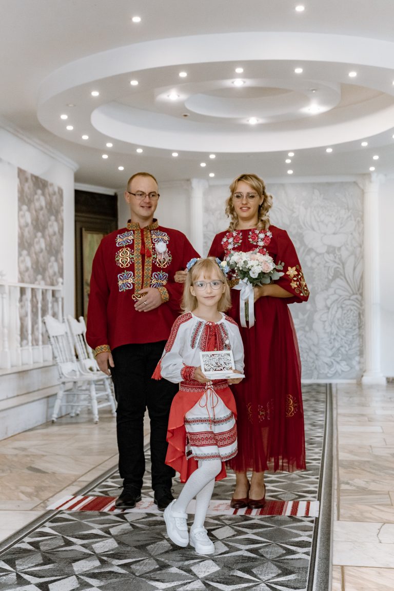 Веронічка тримає коробочку для обручок, а Марина та Ігор стоять позаду в залі РАЦСу