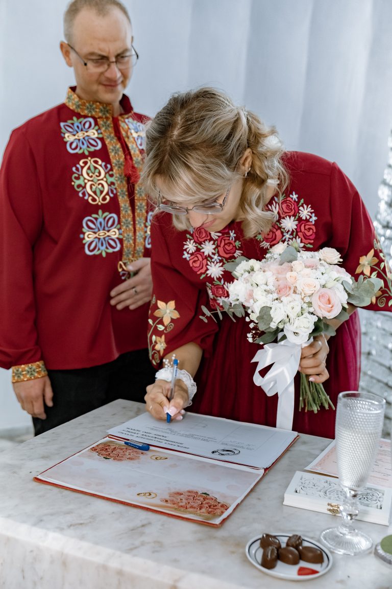 Марина підписує документи про шлюб, тримаючи весільний букет, а Ігор стоїть поруч