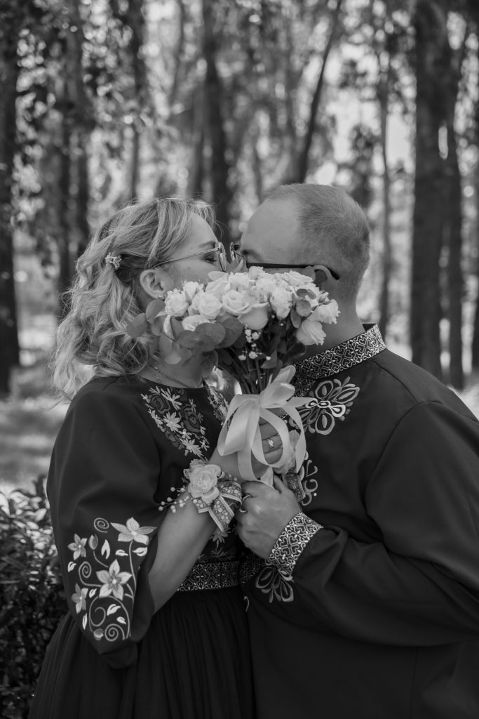 Чорно-білий портрет Марини та Ігоря, які цілуються за весільним букетом у парку