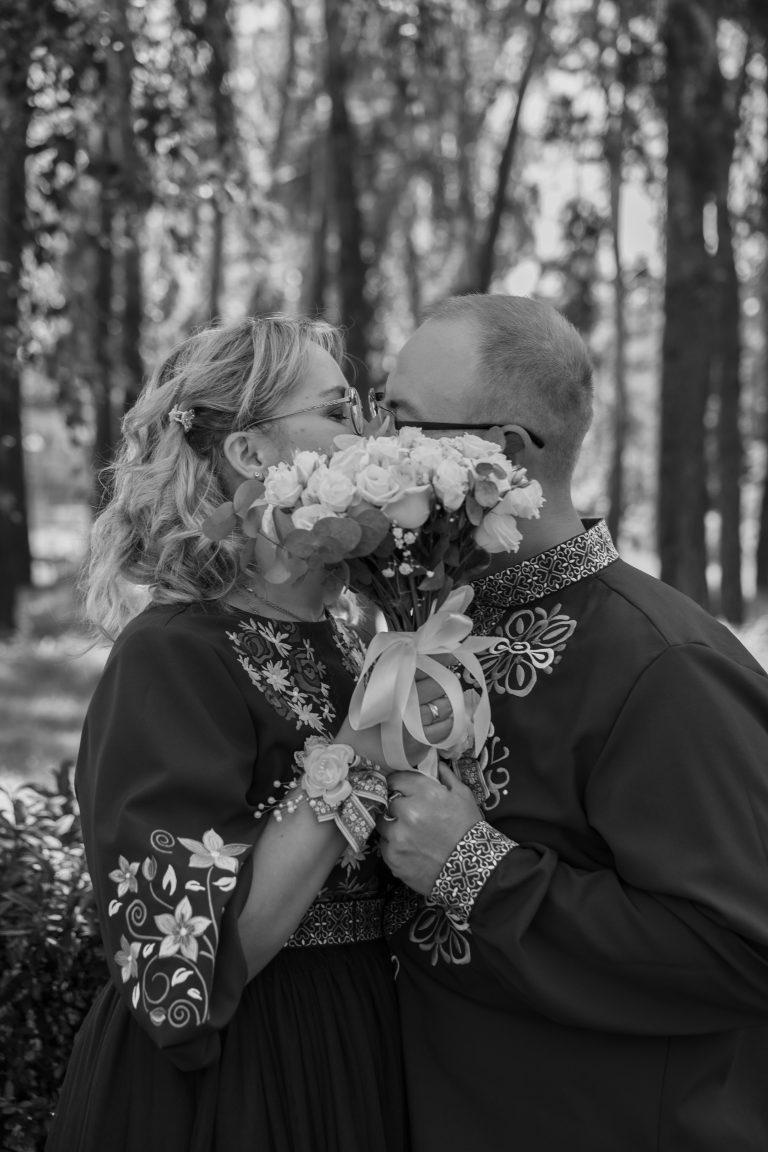 Чорно-білий портрет Марини та Ігоря, які цілуються за весільним букетом у парку