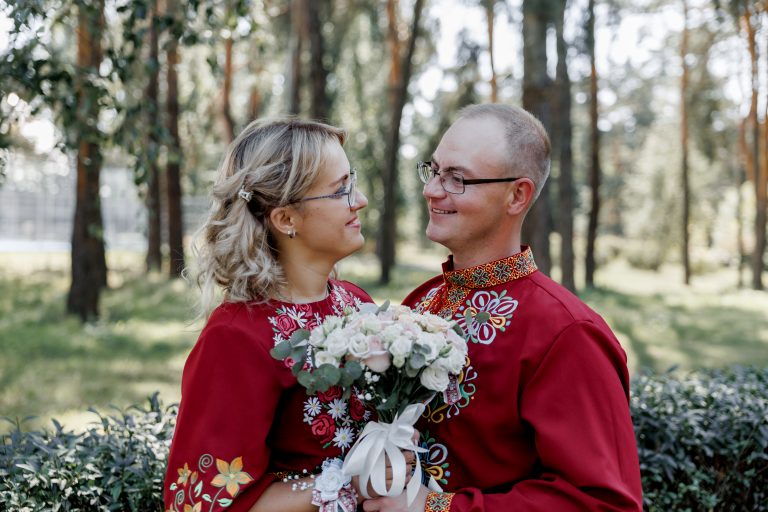 Марина та Ігор сидять поруч у парку та дивляться одне на одного, тримаючи весільний букет
