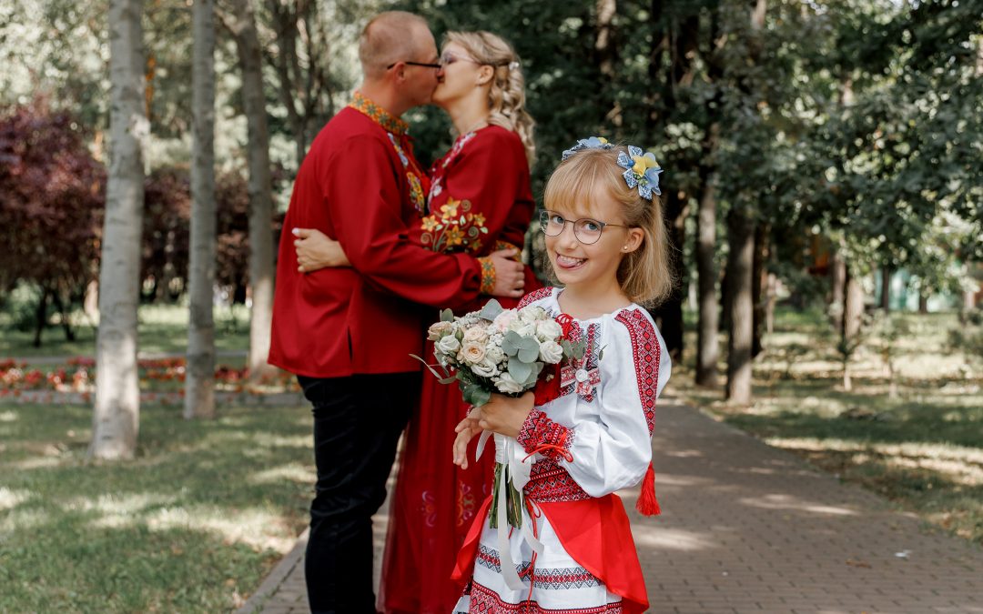 Веронічка у вишиванці стоїть із весільним букетом у парку, Марина та Ігор цілуються позаду, Київ