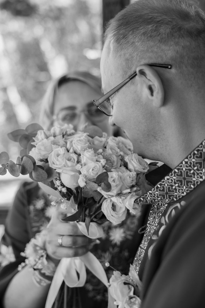 Чорно-білий кадр Ігоря з весільним букетом у руках, Марина розмита на задньому плані