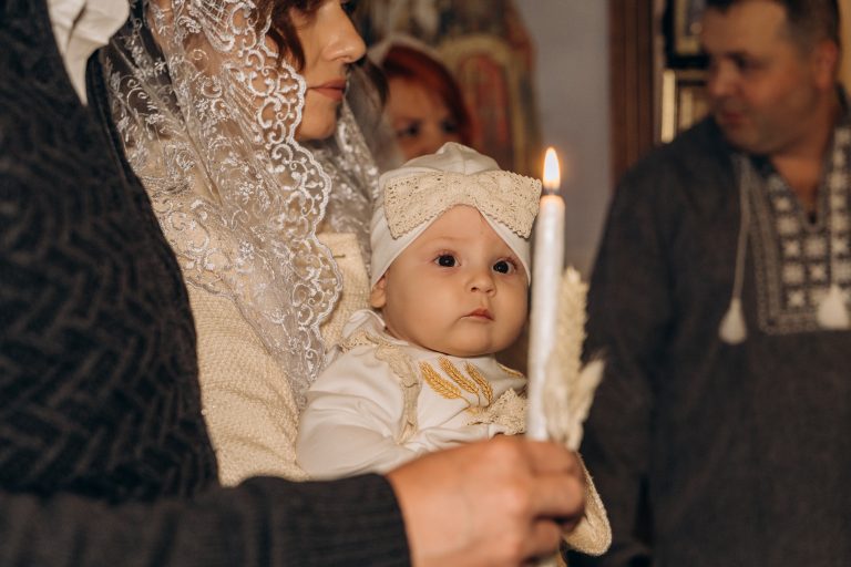 Уляна на руках у жінки біля запаленої свічки під час церковного обряду