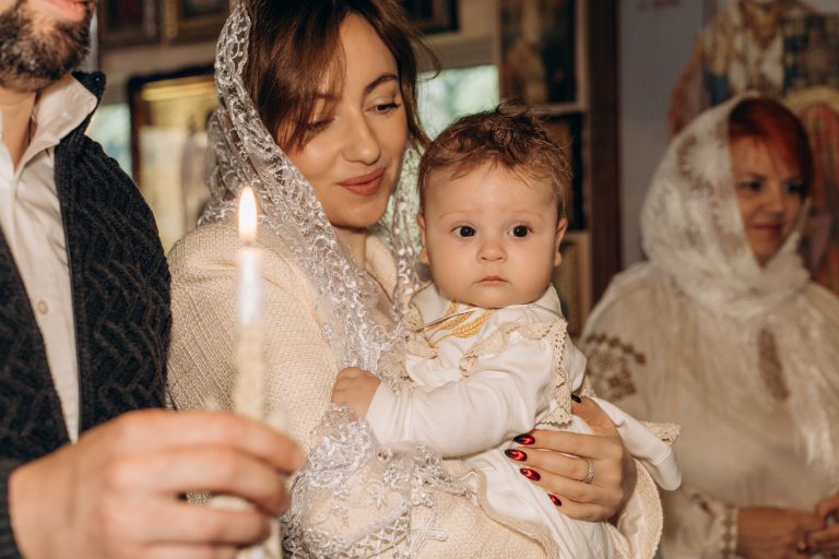 Жінка тримає Уляну на руках поруч із запаленою свічкою під час хрещення