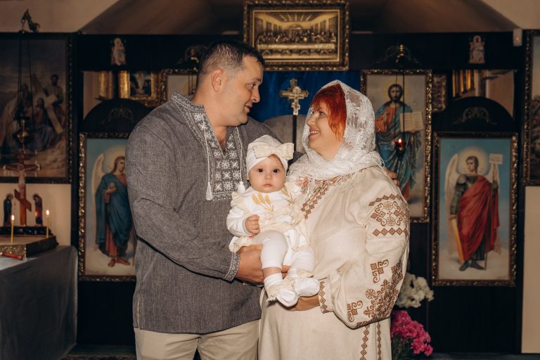 Чоловік і жінка тримають Уляну в центрі кадру на тлі ікон у храмі